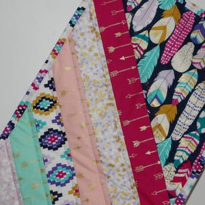 May include: A multi-colored fabric quilt with a patchwork design. The quilt features a variety of patterns, including geometric shapes, arrows, and feathers. The quilt is made with a variety of fabrics, including pink, blue, green, and white.