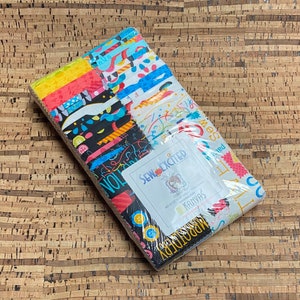 May include: A pack of 12 fat quarter fabric squares featuring a colorful, abstract design with a variety of patterns and colors. The fabric is packaged with a Sew Excited label and the text "Kanvas" on the front.