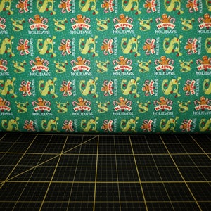 Pode incluir: Tecido verde com um padrão repetido de homens de gengibre segurando bengalas de caramelo e uma faixa que diz "Boas Festas".