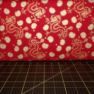 May include: Red fabric with a gold dragon pattern. The fabric is covered in small white flowers.