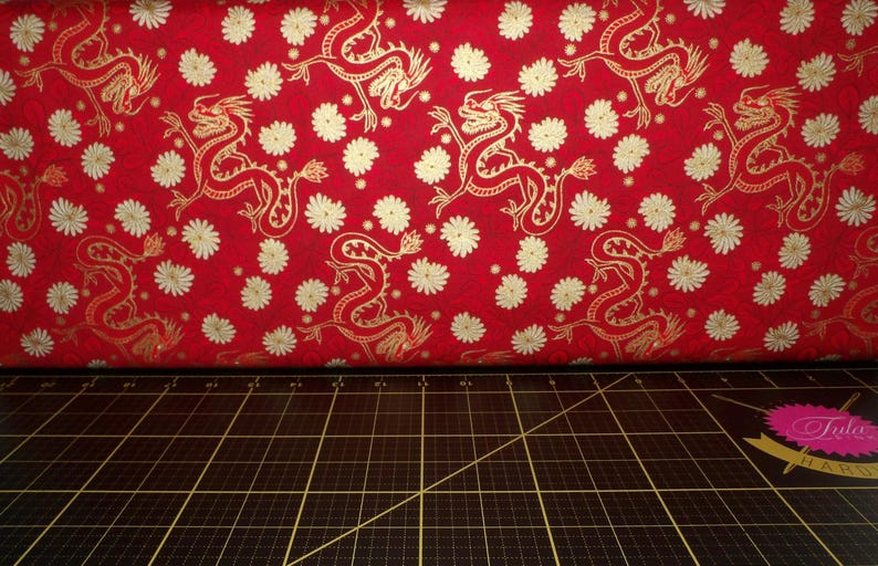 May include: Red fabric with a gold dragon pattern. The fabric is covered in small white flowers.