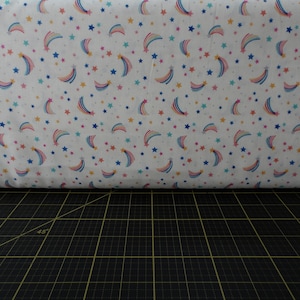 May include: White fabric with a repeating pattern of colorful shooting stars and small white stars.