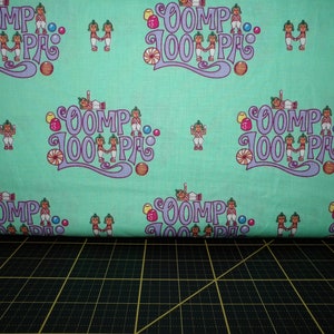Puede incluir: Tela verde con un patrón repetido de Oompa Loompas cogidos de la mano y el texto "Oomp 100 Pa".