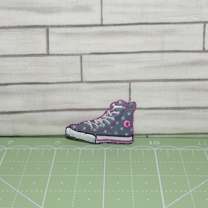 May include: A gray and white high-top sneaker with pink accents and a white star on the side. The sneaker is embroidered on a fabric patch.