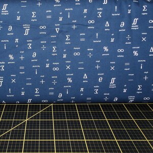 Könnte beinhalten: Ein blauer Stoff mit weißen mathematischen Symbolen darauf gedruckt. Der Stoff ist in der Mitte gefaltet und die untere Kante liegt auf einer schwarzen Schneidematte mit gelben Linien.