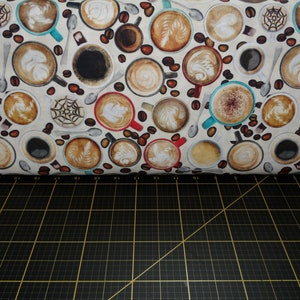 May include: A white fabric with a repeating pattern of coffee cups filled with different types of coffee drinks. The cups are surrounded by coffee beans.