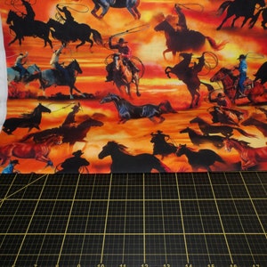 Op de afbeelding: Een kleurrijke stof met een herhalend patroon van cowboys die op paarden rijden tegen een zonsondergang achtergrond. De cowboys zijn gesilhouetteerd en de paarden zijn bruin, zwart en wit.