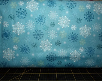 May include: Blue fabric with a white snowflake pattern. The fabric is folded over a black cutting mat.