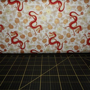 May include: White fabric with a repeating pattern of red dragons and gold floral designs.