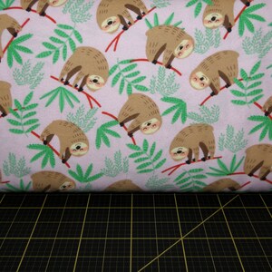 May include: Pink fabric with a repeating pattern of brown sloths hanging from branches with green leaves.