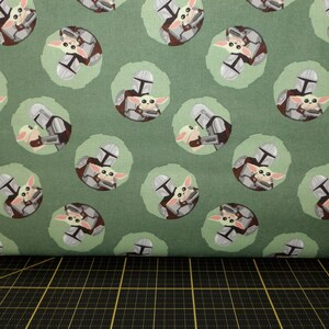 Camelot Fabrics. Star Wars Mandalorian. Mando and Child Toss Green