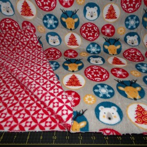 Könnte beinhalten: Ein grauer Stoff mit einem sich wiederholenden Muster aus roten, weißen und blauen Kreisen. Die Kreise zeigen Bilder von einem Reh, einem Eisbären, einem Weihnachtsbaum und Schneeflocken. Der Stoff ist umgeklappt, um ein rotes und weißes geometrisches Muster zu zeigen.