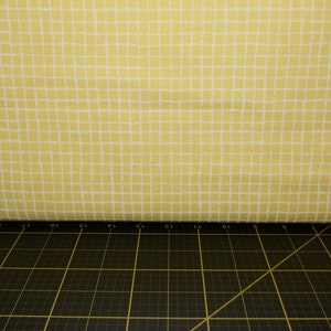 May include: A yellow fabric with a white grid pattern. The fabric is folded over a black cutting mat.