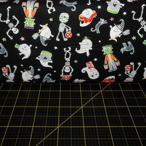 May include: Black fabric with a Halloween-themed print featuring ghosts, skeletons, mummies, witches, and monsters. The fabric is on a black cutting mat.