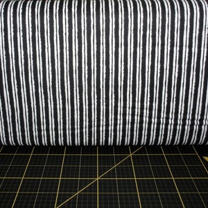 May include: Black and white striped fabric with a slightly textured surface. The fabric is folded in half and lying on a black and gold cutting mat.