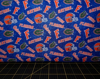 Może przedstawiać: Niebieski materiał z powtarzającym się wzorem logo Florida Gators. Logo zawiera litery "F" i "Gators", głowę aligatora i kask do futbolu amerykańskiego. Wzór zawiera również tekst "Pride" i "Florida".