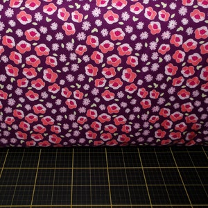 May include: Purple fabric with a repeating pattern of pink and orange flowers. The flowers are surrounded by small white flowers and green leaves.