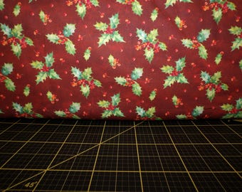 May include: Red fabric with a repeating pattern of green holly leaves and red berries.