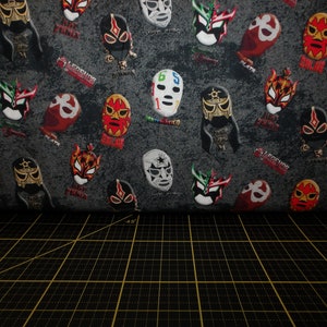 Puede incluir: Una tela gris con un patrón repetido de máscaras de lucha libre coloridas. Las máscaras son de varios estilos y colores, incluyendo rojo, negro, verde y blanco. La tela tiene las palabras "Legend", "Big Panda" y "Milan" impresas en ella.
