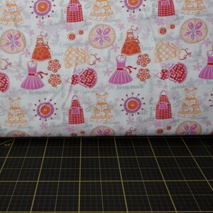 Puede incluir: Tela blanca con un patrón repetido de delantales, vestidos y diseños florales en tonos rosa, naranja y rojo. Las palabras "homemade", "cupcake", "tea" y "flour" están impresas. Ideal para proyectos de costura y manualidades.