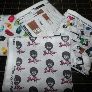 May include: Four pieces of fabric featuring Bob Ross, the Joy of Painting, and paintbrushes. The fabric is white with a repeating pattern of Bob Ross's face and the words "Bob Ross" in red. The fabric is 100% cotton.