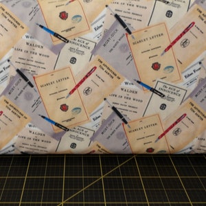 May include: A beige fabric with a repeating pattern of book covers and pens. The book covers feature titles like "The Adventures of Tom Sawyer", "Moby Dick", "Walden", "The Age of Innocence", and "Scarlet Letter".