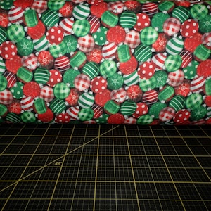 May include: A close-up of a fabric with a repeating pattern of red and green Christmas ornaments. The ornaments are decorated with white stripes, polka dots, and plaid patterns.
