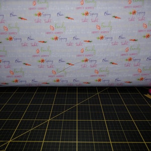 May include: A light blue fabric with a repeating pattern of pink flowers, green leaves, orange carrots, and the text "Hippity Hoppity Spring Bloom Tikit Takit Family".