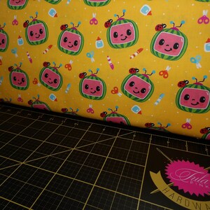 May include: Yellow fabric with a repeating pattern of cartoon watermelon TVs with smiling faces, ladybugs, and school supplies.
