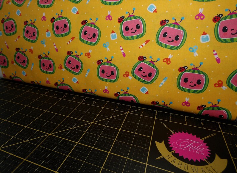 May include: Yellow fabric with a repeating pattern of cartoon watermelon TVs with smiling faces, ladybugs, and school supplies.
