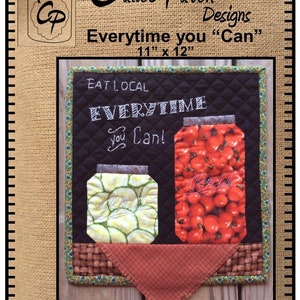 May include: A quilted wall hanging with a black chalkboard background featuring the text "EAT LOCAL EVERYTIME You Can!" and two jars of preserved food. The jars are filled with red tomatoes and green pickles. The hanging is 11 inches by 12 inches.