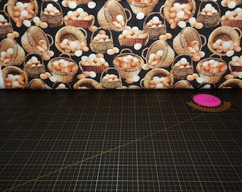 May include: Fabric with a repeating pattern of brown woven baskets filled with brown and white eggs on a black background. Some eggs are scattered around the baskets. The fabric is on a black cutting mat.