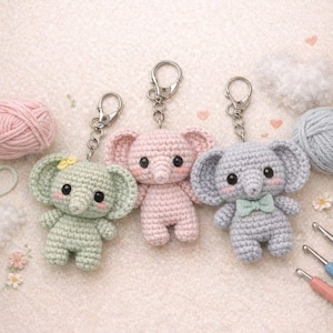 May include: Three handmade crochet elephant keychains in pastel colors: mint green, pink, and gray. Each elephant has large ears, a trunk, and a silver keychain clasp. The gray elephant has a small bow tie. Yarn and crochet hooks are in the background.