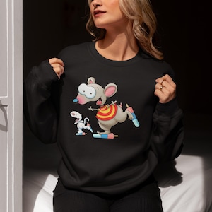 Pode incluir: Camisola preta de gola redonda com um personagem de rato de desenho animado com um colete listrado vermelho, amarelo e branco e um picolé. Um cão de desenho animado branco menor também é apresentado. A camisola é feita de um material macio.