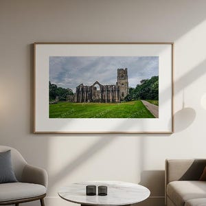 Pode incluir: Uma impressão emoldurada de uma histórica ruína de abadia de pedra, contra um céu nublado e grama verde exuberante. A obra de arte é exibida em uma sala de estar, com uma paleta de cores neutras e mobiliário moderno.
