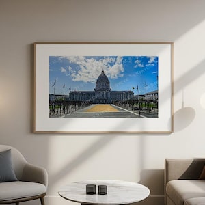 May include: A framed photograph of a large building with a domed roof, set against a blue sky with fluffy white clouds. The building has a classical design, with flags and a long walkway leading to the entrance. The photograph is displayed in a living room setting.