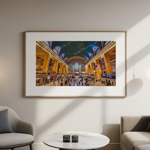 May include: A framed print of Grand Central Terminal in New York City, showcasing the iconic architecture and bustling atmosphere. The image captures the grand hall with its high ceilings, arched windows, and numerous people. The artwork is displayed in a living room setting.