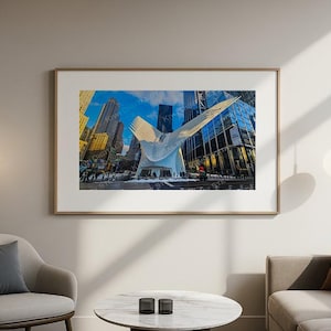 May include: A framed print of a modern architectural structure with a white, wing-like design, set against a backdrop of tall buildings and a bright blue sky. The artwork is displayed in a living room setting.