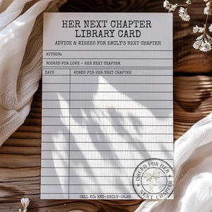 Könnte beinhalten: Eine Bibliothekskarte mit dem Text "HER NEXT CHAPTER LIBRARY CARD" aufgedruckt. Die Karte enthält Felder für Autor, Datum und Wünsche. Die Karte ist von weißem Stoff und Blumenzweigen auf einer Holzoberfläche umgeben.
