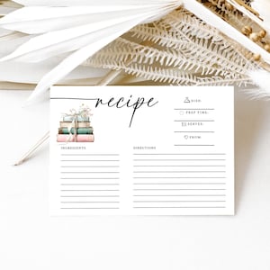 Puede incluir: Una tarjeta de recetas rectangular blanca con la palabra recipe en letra cursiva negra en la parte superior. La tarjeta incluye una pequeña ilustración de una pila de libros atados con una cuerda, junto con líneas impresas para ingredientes y pasos.