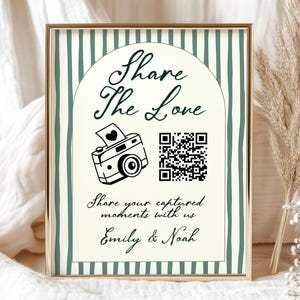 Op de afbeelding: Een ingelijst bord met de tekst "Share The Love" en een camera-afbeelding. Het bord heeft een crèmekleurige achtergrond met groene verticale strepen en een gouden rand. Daaronder staat de tekst "Share your captured moments with us Emily & Noah."