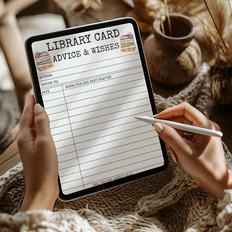 May include: A digital tablet displaying a "LIBRARY CARD ADVICE & WISHES" template. The template includes fields for author, recipient, date, and space for "WORDS FOR HER NEXT CHAPTER." The tablet is held by a person, with a stylus poised above the screen.