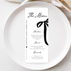 Könnte beinhalten: Eine vertikale weiße Menükarte mit schwarzem Text und einer schwarzen Schleifengrafik. Der Text lautet The Menu, Starters, Mains, Desserts und Josephine's Bridal Shower 2026. Das Menü listet Speisen wie Burrata, Smoked Salmon und Tiramisu auf.