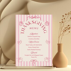 Pu&ograve; includere: Un menu di ringraziamento con uno sfondo a righe rosa e bianche. Il menu comprende antipasti, piatti principali e dessert. Il testo "Thanksgiving Menu" &egrave; in alto in un carattere decorativo. Sono presenti anche zucche e ghiande decorative.