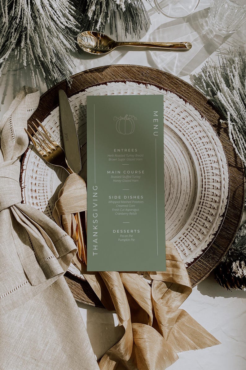 May include: A Thanksgiving menu card in sage green with a pumpkin illustration, placed on a layered plate setting. Gold cutlery and a linen napkin complement the autumnal theme. The menu lists entrees, main course, side dishes, and desserts.