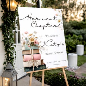Peut inclure: Un panneau rectangulaire blanc avec le texte Her next Chapter, Welcome to Katy's Bridal Shower, 45 DAYS BEFORE THE BIG DAY et 01.01.2030. Le design présente une pile de cinq livres colorés attachés par un ruban et des motifs floraux.