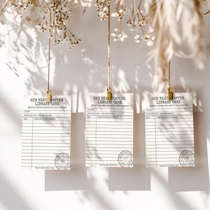 Three library card advice templates hang from twine with gold clips against a white wall with floral shadows.