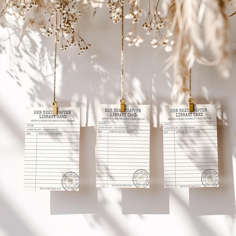 Three library card advice templates hang from twine with gold clips against a white wall with floral shadows.
