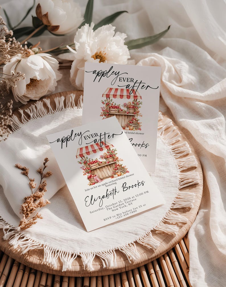 Puede incluir: Dos tarjetas de invitaci&oacute;n rectangulares blancas con el texto "appley EVER after" en caligraf&iacute;a negra. Las tarjetas muestran una ilustraci&oacute;n en acuarela de un puesto de manzanas de madera con un toldo a rayas rojas y blancas, lleno de manzanas.