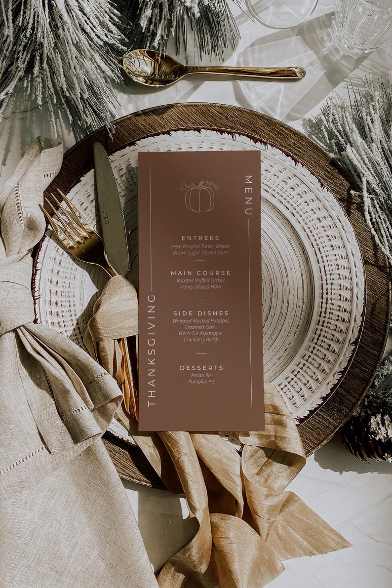 May include: Thanksgiving menu card on a plate with a fork and knife. The menu is brown with a pumpkin illustration and lists entrees, main course, side dishes, and desserts. The plate is set with a gold fork and knife, and a beige napkin.